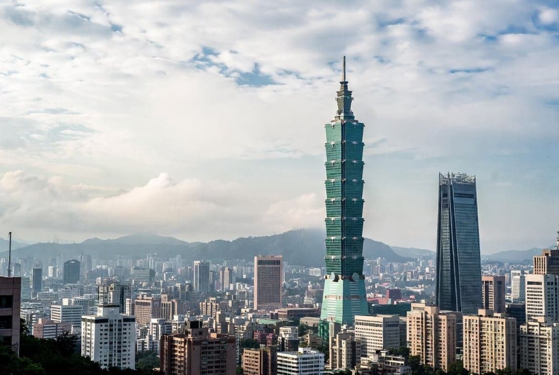 Taipei cityscape with Taipei 101 tower rising above lower buildings and green mountains in the background under hazy sky